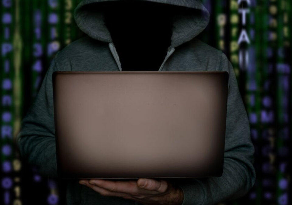 Hacker with laptop stands against the backdrop