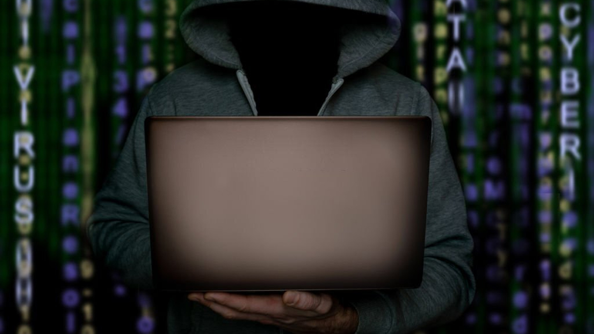 Hacker with laptop stands against the backdrop