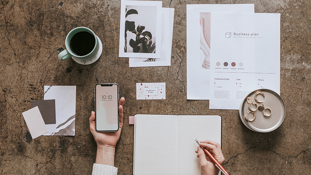 Woman holding a mobile phone mockup writing while a business plan