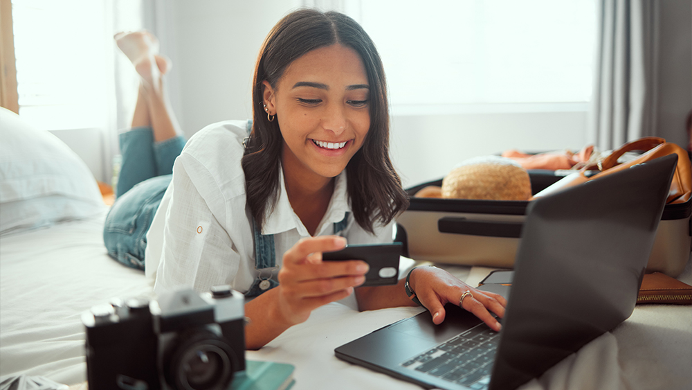 Woman lied down in front of laptop and looking at a card in her hand